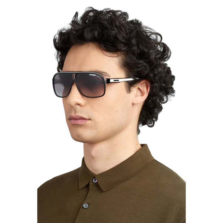 A man with curly dark hair wearing Fendi aviator sunglasses with a silver-tone frame and dark lenses, paired with an olive brown polo shirt, against a plain white background.