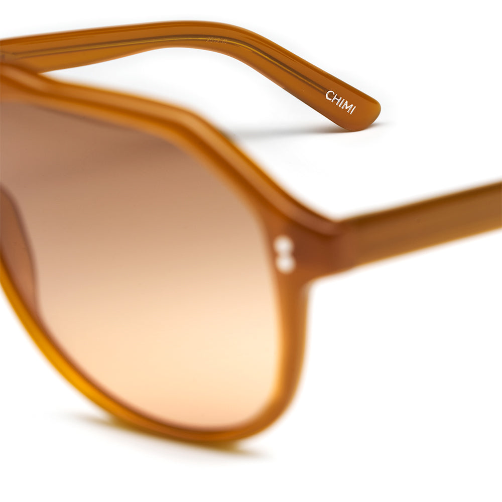 Close-up of amber acetate aviator-style sunglasses with a warm gradient lens and the brand name CHIMI printed on the temple arm, set against a clean white background.